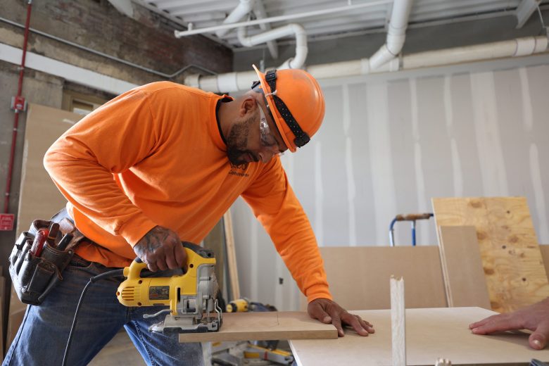 Darrell Williams usa una sierra con una camisa naranja de manga larga y un casco naranja.