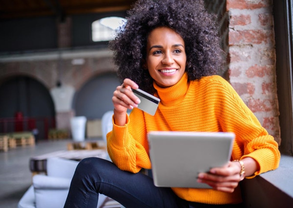 Una mujer afroamericana felizmente usa su tarjeta de crédito para hacer una compra en línea.