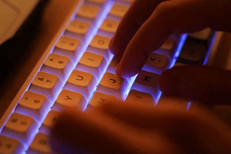 Las manos escriben en un teclado de computadora iluminado.