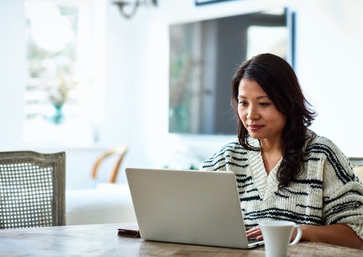 Una mujer sentada en su mesa de comedor y escribiendo en su computadora portátil.