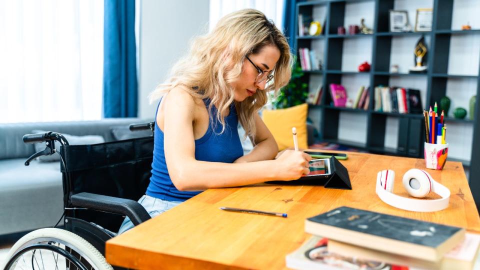 Una empresaria sentada en silla de ruedas trabaja con una tableta digital en el lugar de trabajo.