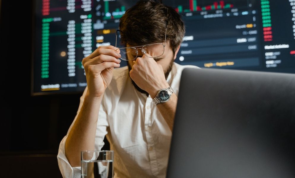 hombre frotándose los ojos mientras está sentado frente a la computadora portátil