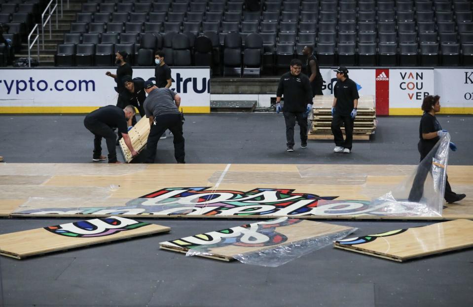 Los empleados cambian las superficies de juego de Crypto.com Arena de madera dura después de un juego de los Clippers por la tarde a hielo.