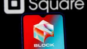 El logotipo de Block (SQ) se muestra en la pantalla de un teléfono con el antiguo nombre y logotipo de la empresa, Square, visible detrás del teléfono.