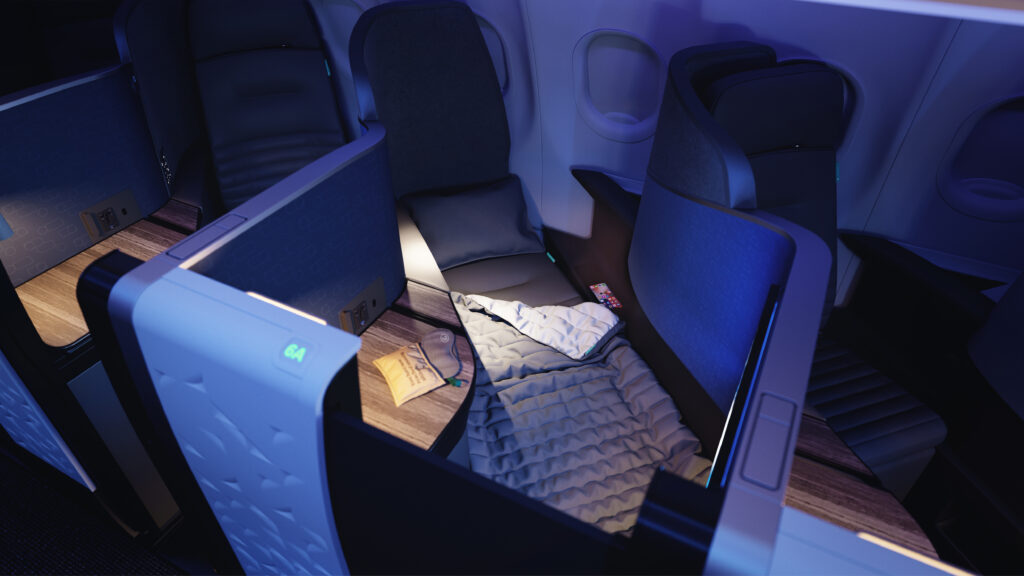 La mini suite de clase ejecutiva de JetBlue, con el asiento completamente plano, con iluminación LED azul que emite un brillo tranquilo.  Un kit de amenidades se sienta en la mesa al lado de la cama.