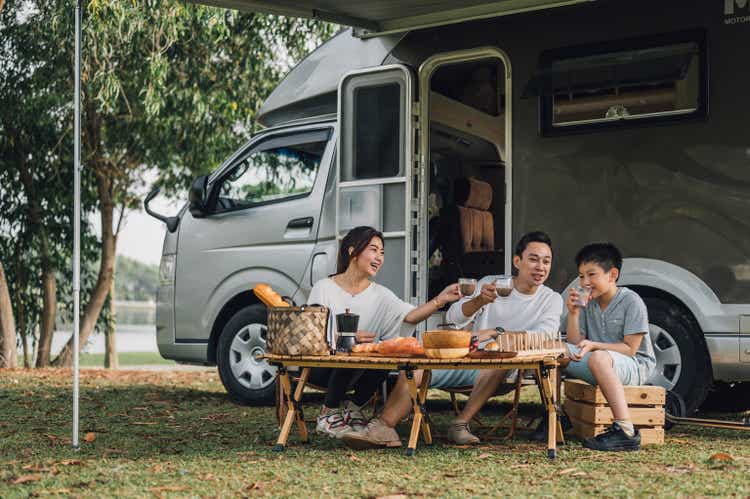 Feliz familia asiática hablando en una mesa de picnic junto al remolque de la caravana en la naturaleza