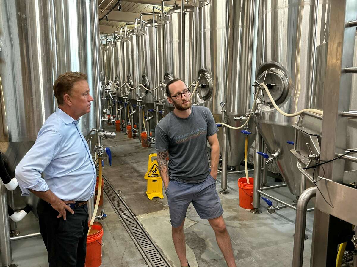 El propietario de New Park Brewing, Alex Dee, le cuenta al gobernador Ned Lamont sobre el amplio sistema de elaboración de cerveza de la cervecería.