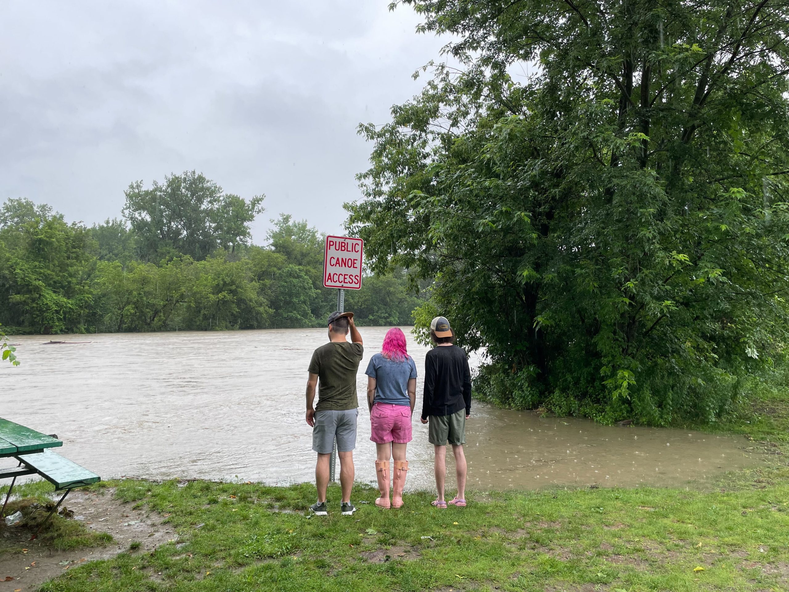 tres personas de pie junto a un río con un cartel delante de ellos.