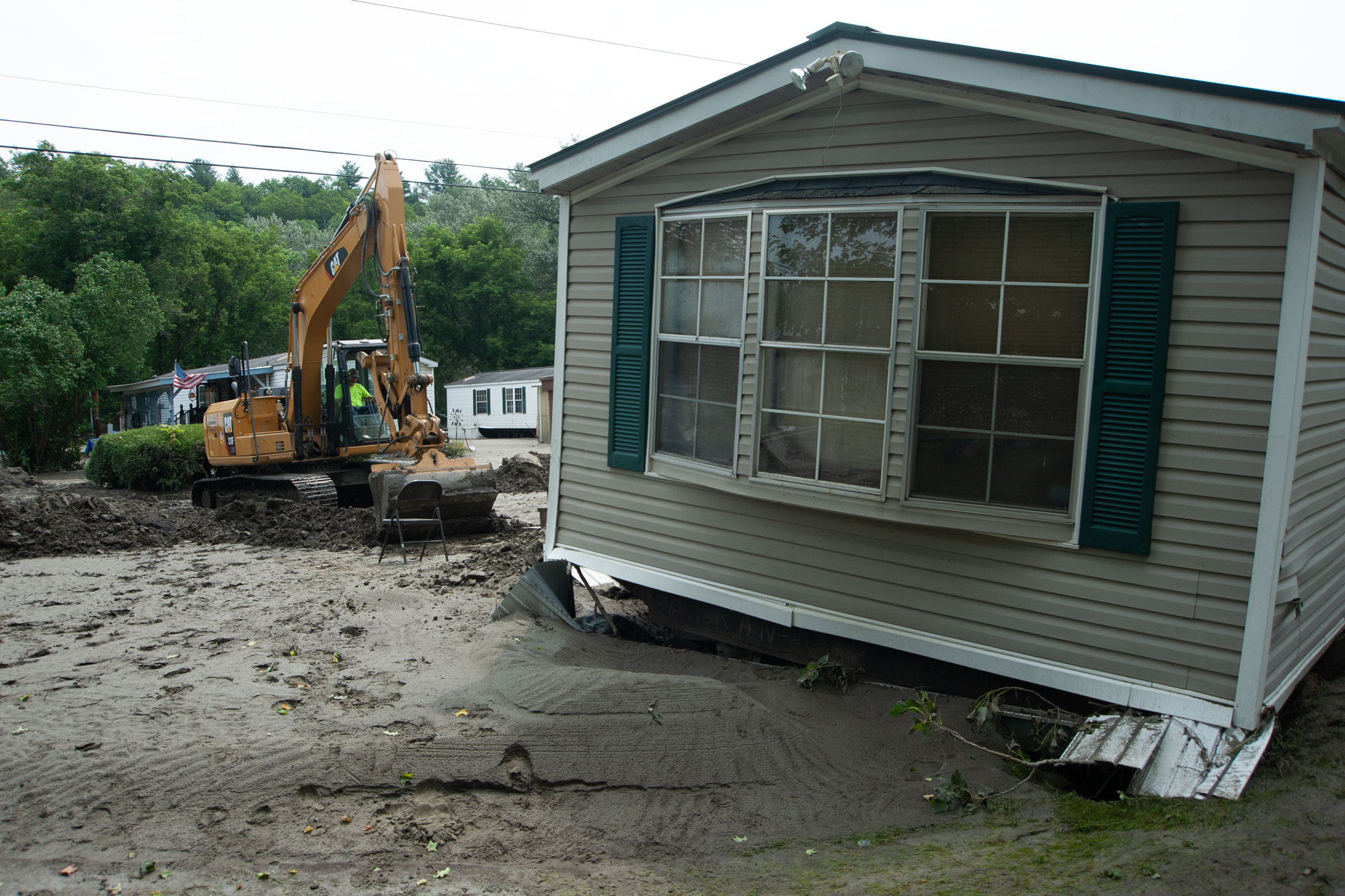 Una excavadora junto a una casa prefabricada en el barro.