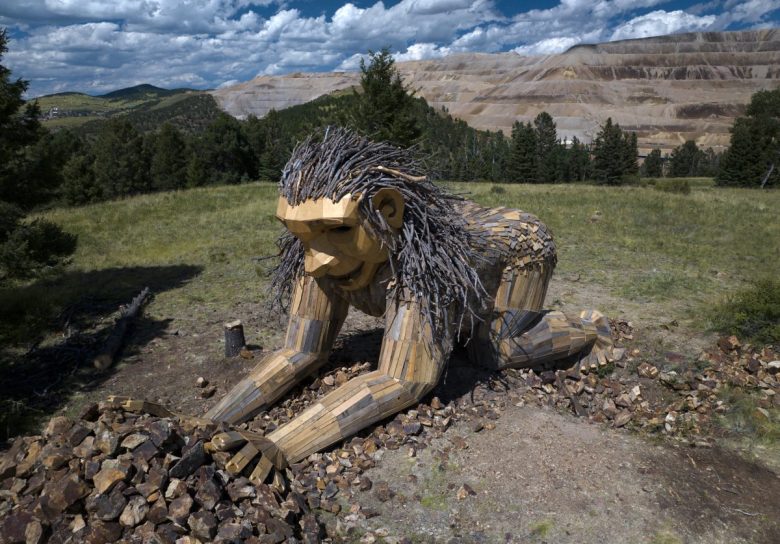 una vista aérea de un troll de madera está agachado junto a un montón de rocas con una mina en el fondo