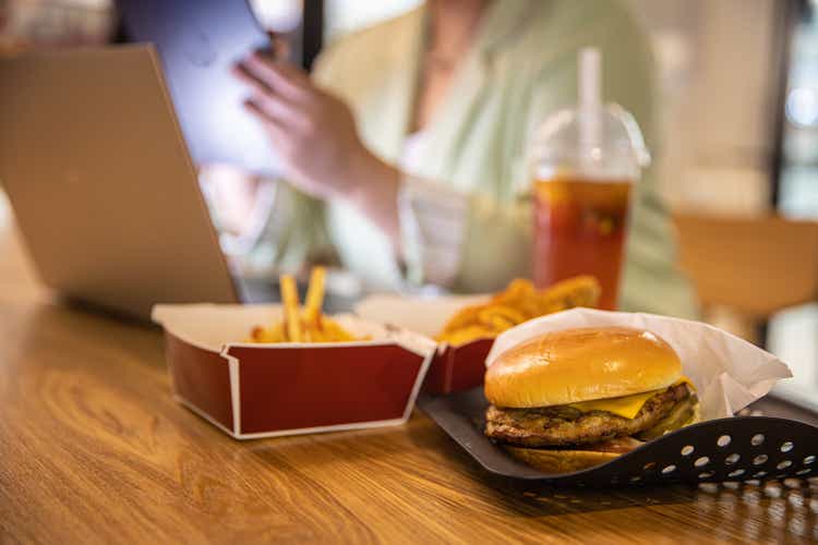 Empresaria que trabaja en la computadora portátil con comida rápida en la mesa del restaurante