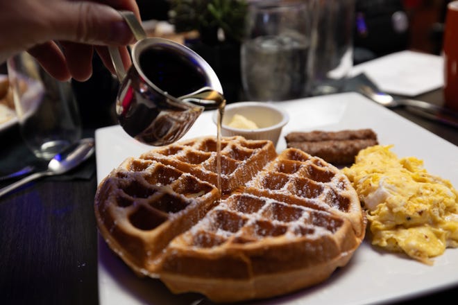 Combo de desayuno servido con waffle belga, huevos revueltos y dos salchichas de Love 66 Bistro.