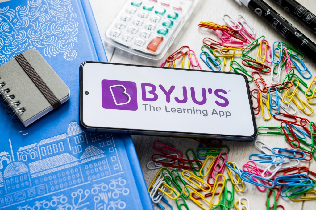 El logotipo de Byju aparece en un teléfono inteligente sobre una mesa cubierta con útiles escolares