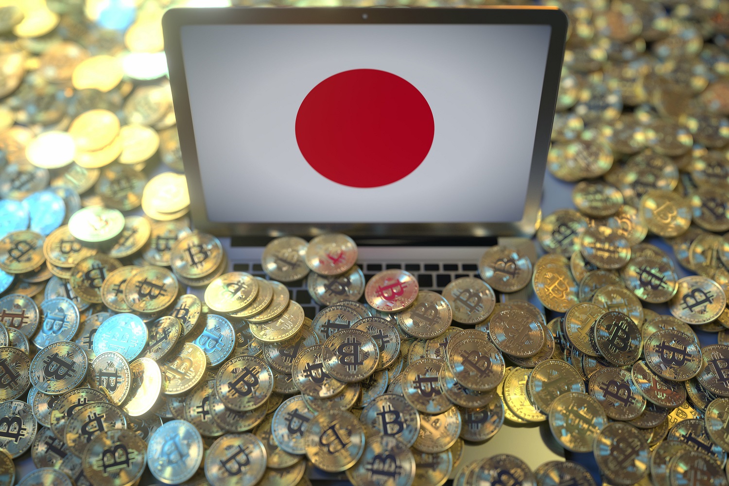 Una gran cantidad de fichas de metal de color dorado destinadas a representar Bitcoins esparcidas alrededor de una computadora portátil en cuya pantalla se muestra la bandera japonesa.