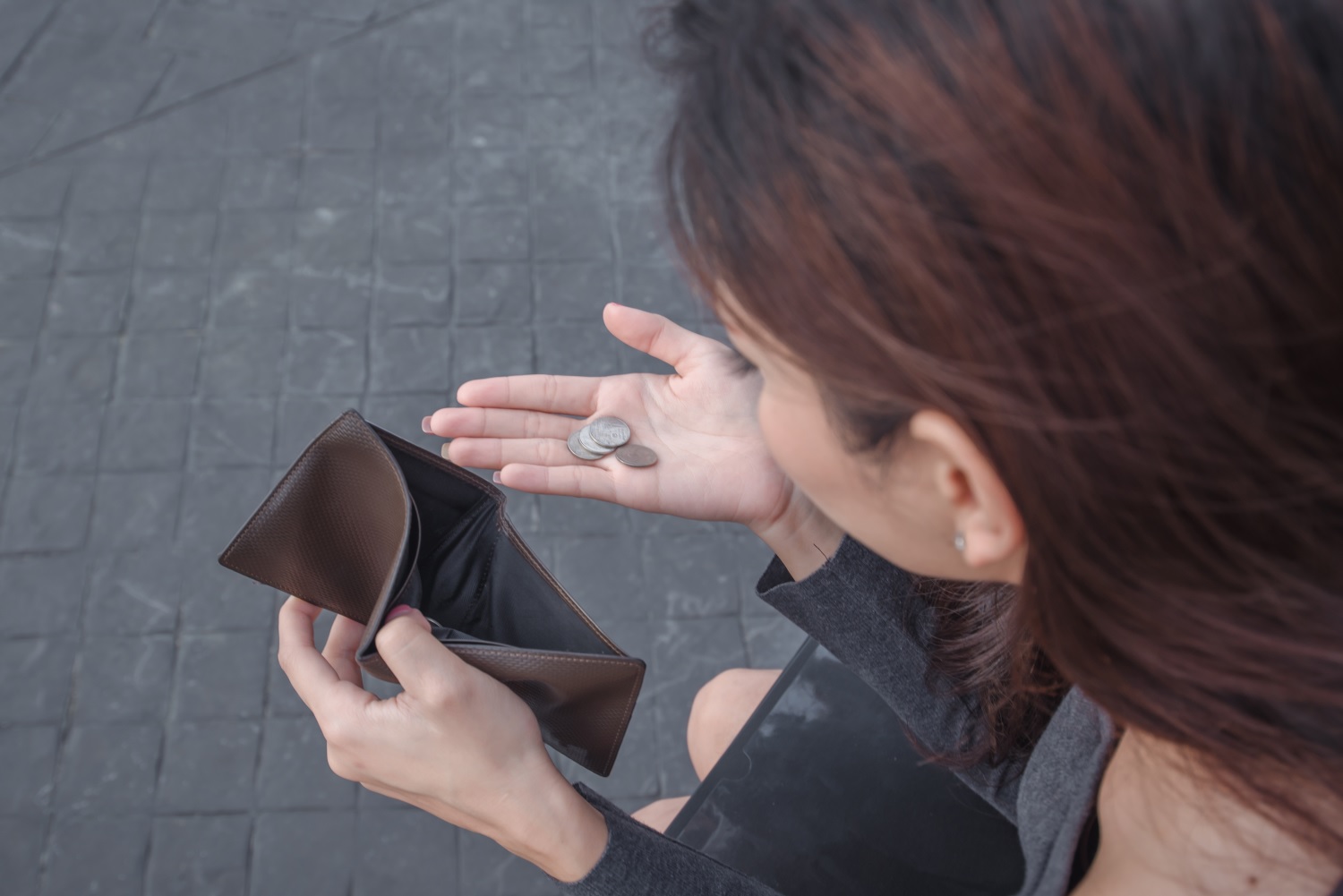 Una mujer sostiene unas cuantas monedas en una mano y una billetera vacía en la otra.