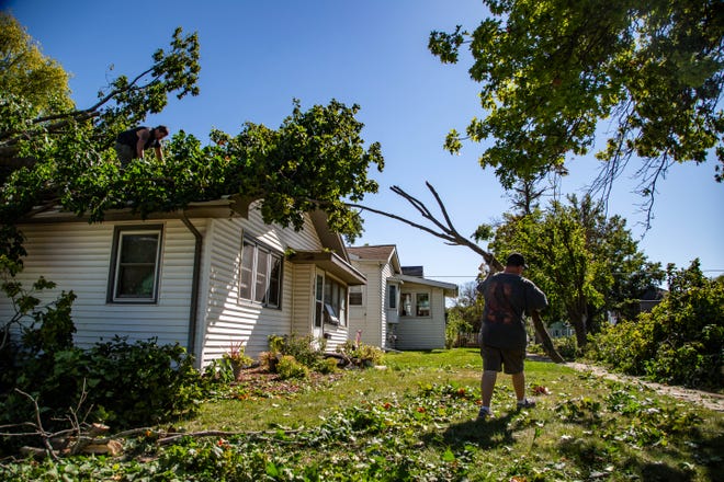 Bruce Rook usa una motosierra para cortar un árbol que cayó sobre la casa de Jerry Eash en Marshalltown mientras Eash mueve las ramas a la acera el martes, 11 de agosto de 2020. Un derecho con vientos de 80 a 100 mph azotó Iowa el día anterior.