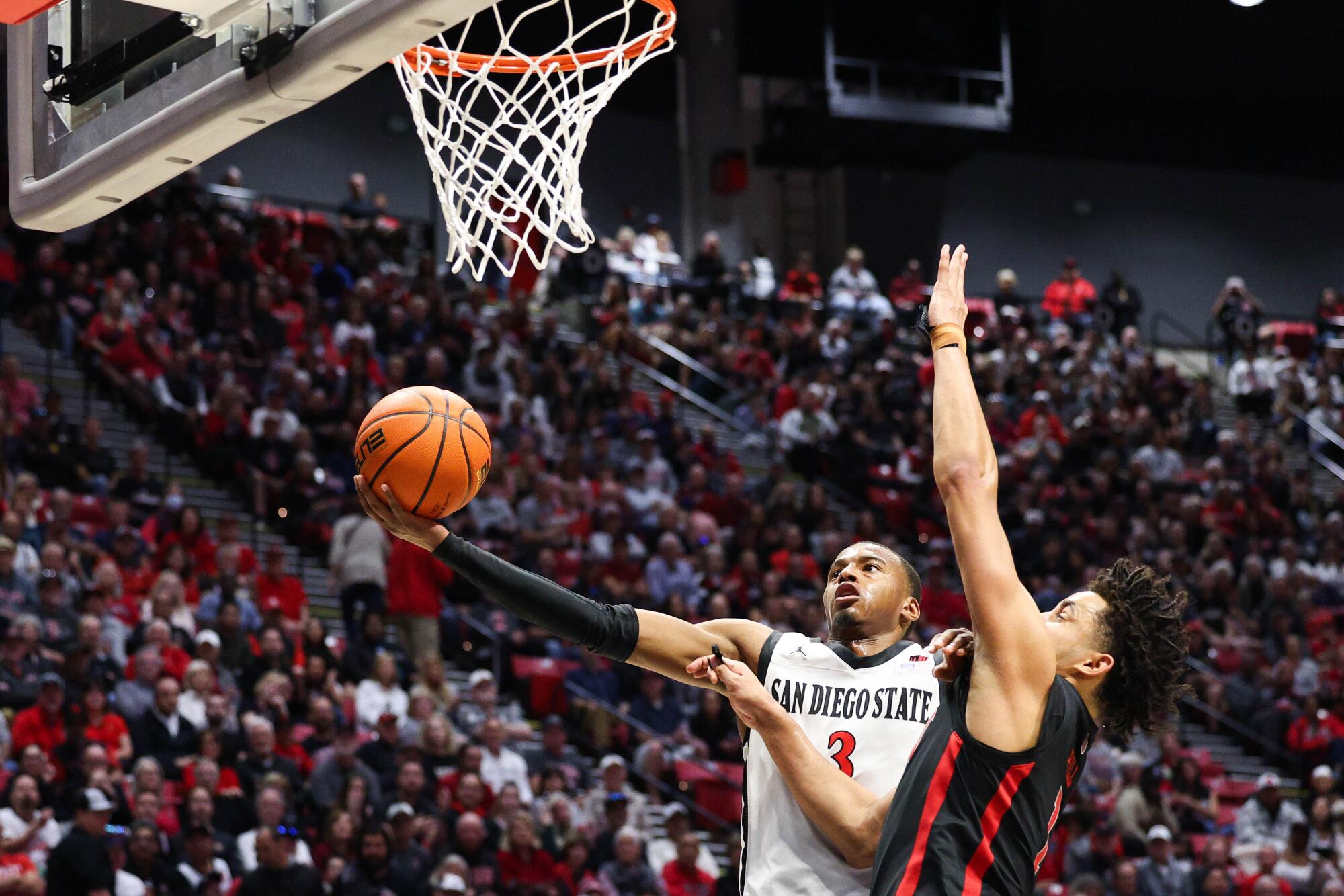 El guardia estatal de San Diego, Micah Parrish (3), dispara contra el delantero de la UNLV, Jalen Hill (1).