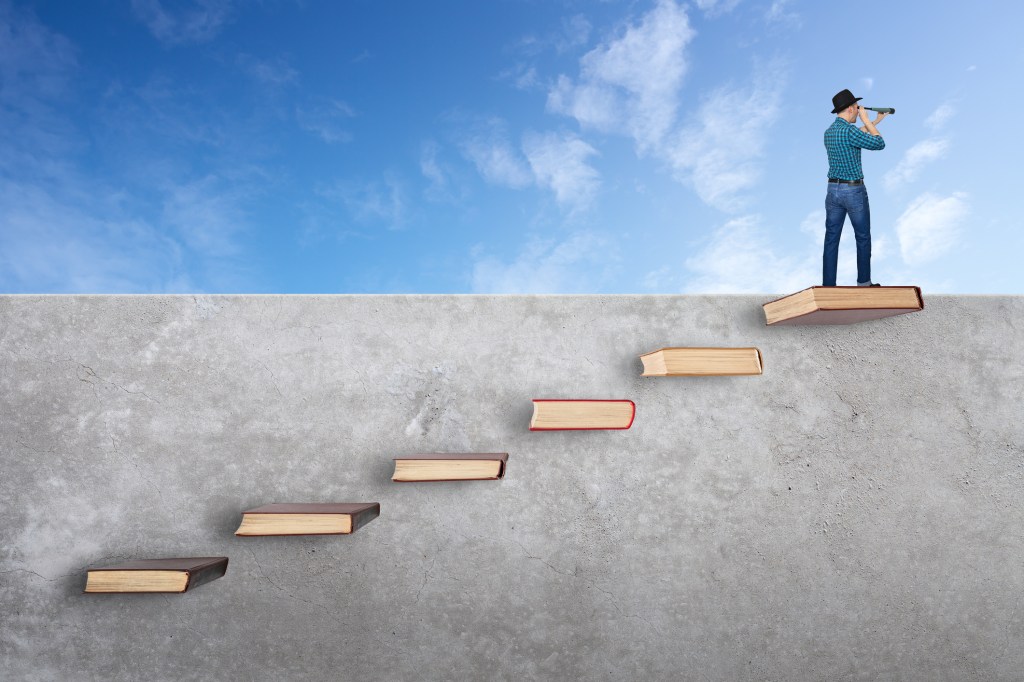 Hombre encima de la pared con libros como escaleras.  Mirando a través del telescopio