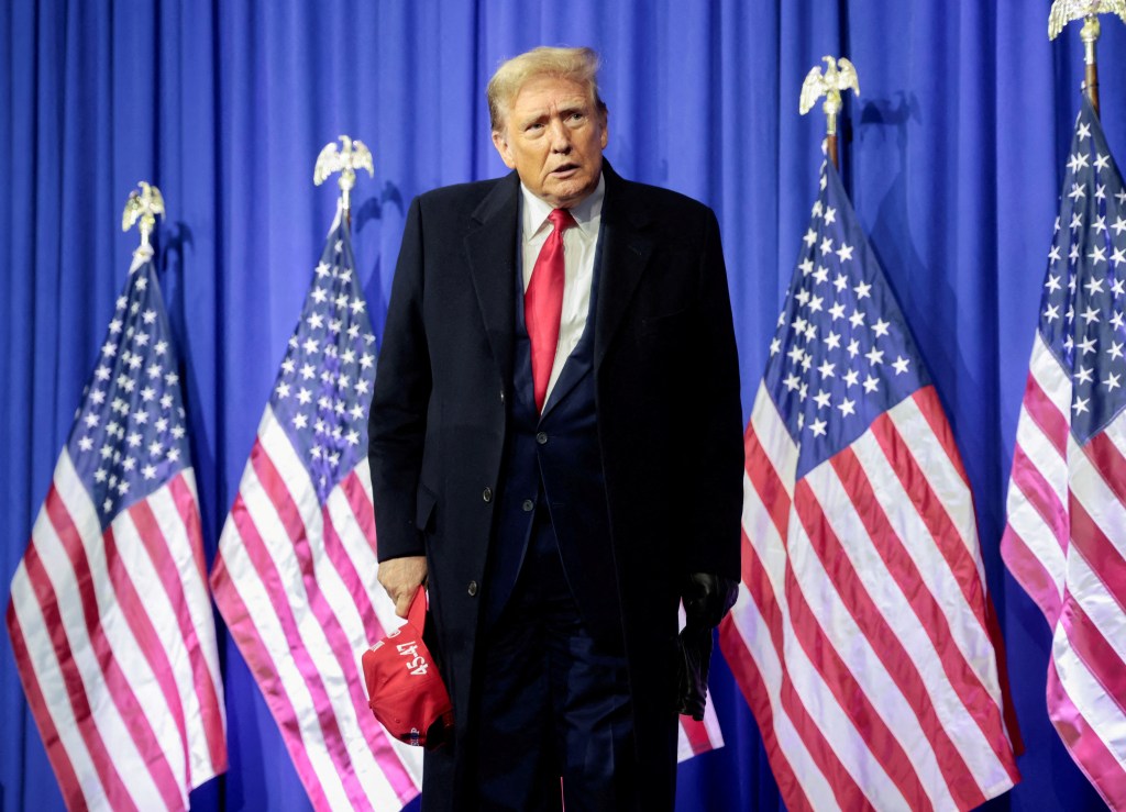 El expresidente estadounidense Donald Trump se encuentra en un podio, hablando por micrófonos frente a un fondo de bandera estadounidense.