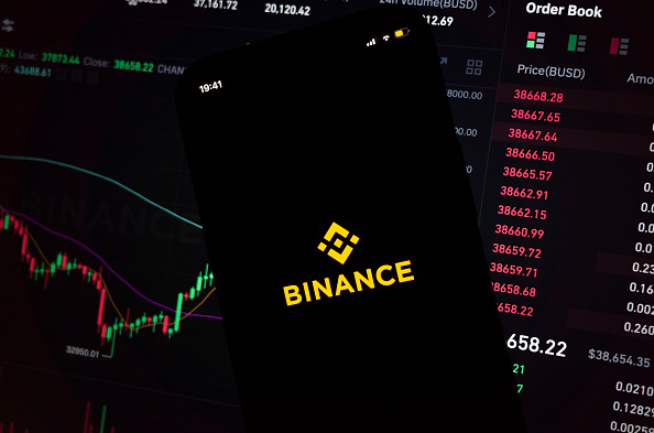 En esta ilustración fotográfica, un iPhone muestra la aplicación y el logotipo de la popular plataforma de intercambio de criptomonedas Binance, con la versión de escritorio de fondo que muestra las tendencias del mercado y los tipos de cambio de la criptomoneda Bitcoin el 8 de marzo de 2022 en Leeds, Reino Unido.  (foto de Daniel Harvey González/In Pictures vía Getty Images)