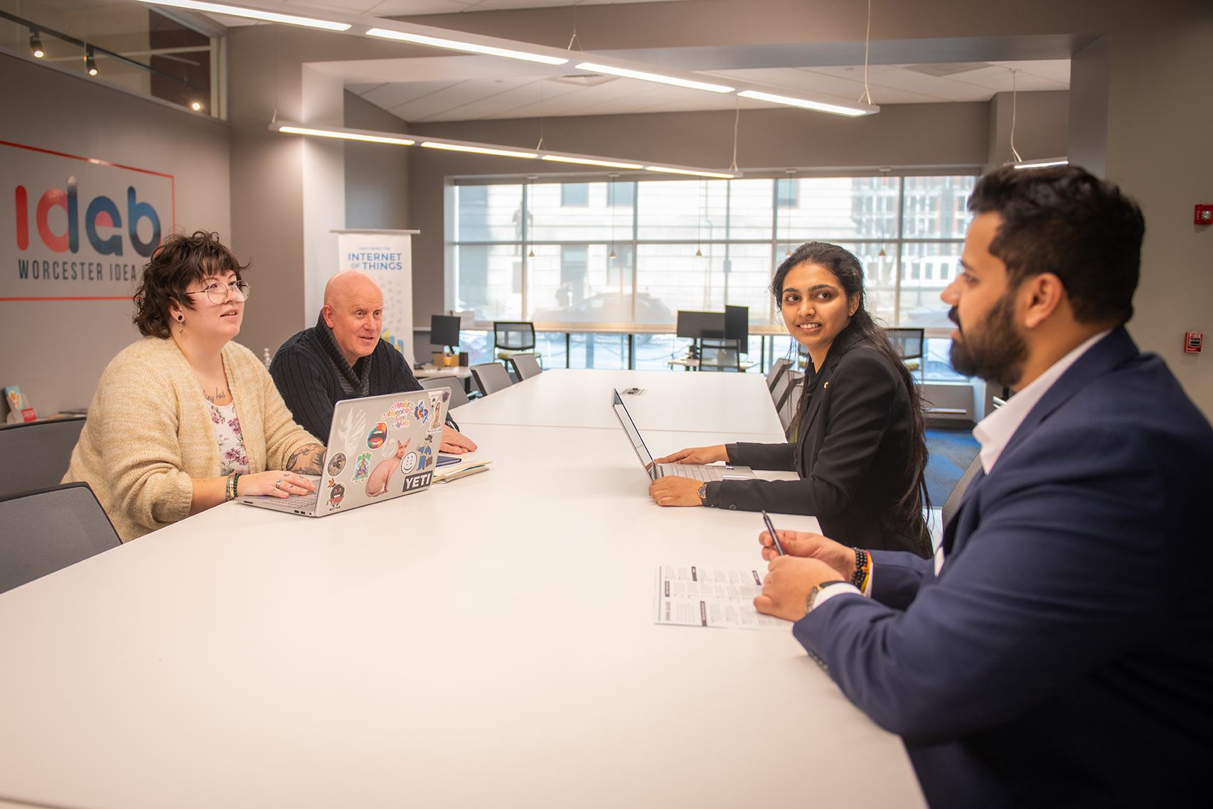 Los estudiantes de la Escuela de Administración Parimala Yerraguntla, MS '25, y Aaryan Pankaj Dabhade, MA '25 (derecha), se reúnen en el Worcester Idea Lab con Margie Breault, Gerente de Avance Empresarial y Comunitario de la Ciudad de Worcester en la Oficina de Desarrollo Económico. y Tom Herald, director del Centro de Desarrollo de Pequeñas Empresas de la Universidad Clark.