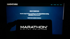 Persona que sostiene un teléfono móvil con el logotipo de la empresa estadounidense Marathon Digital Holdings Inc. en la pantalla frente a la página web.  Centrarse en la pantalla del teléfono.  Foto sin modificar.  acciones de MARA