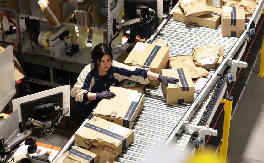 Una trabajadora de Amazon clasifica los pedidos de los clientes en cajas que viajan a lo largo de una cinta transportadora.