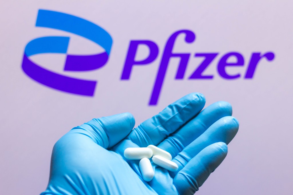 Logotipo de Pfizer visto en la pantalla con pastillas en la mano en una ilustración fotográfica de Rafael Henrique