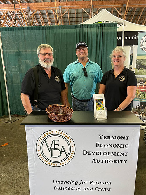 Foto: VEDA en los días de campo y feria del condado de Addison de 2023.  Peter Fitzgerald (izq.) y Ellen Howrigan (der.) con un prestatario de VEDA.  Crédito de la foto VEDA