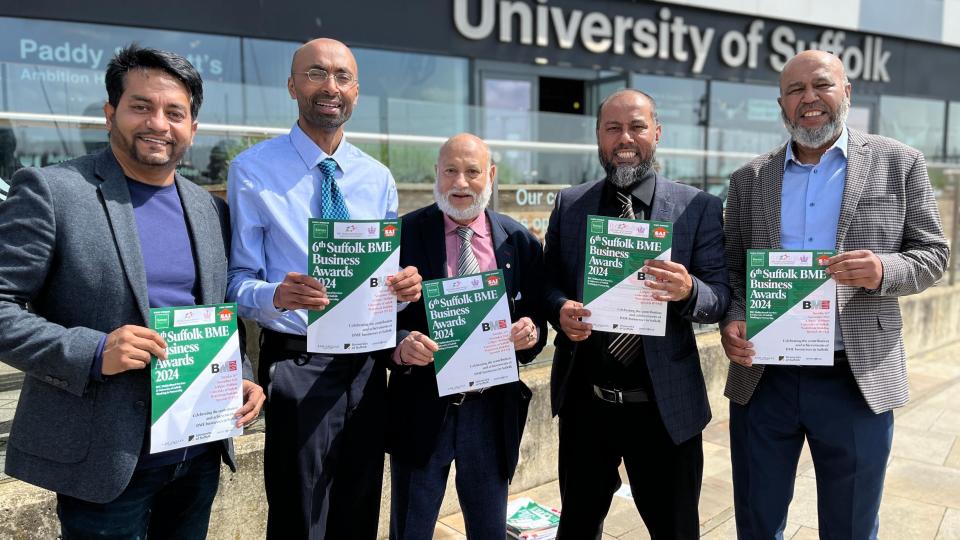 Cinco hombres de ascendencia bangladesí sostienen carteles A4 que promocionan un evento de premiación