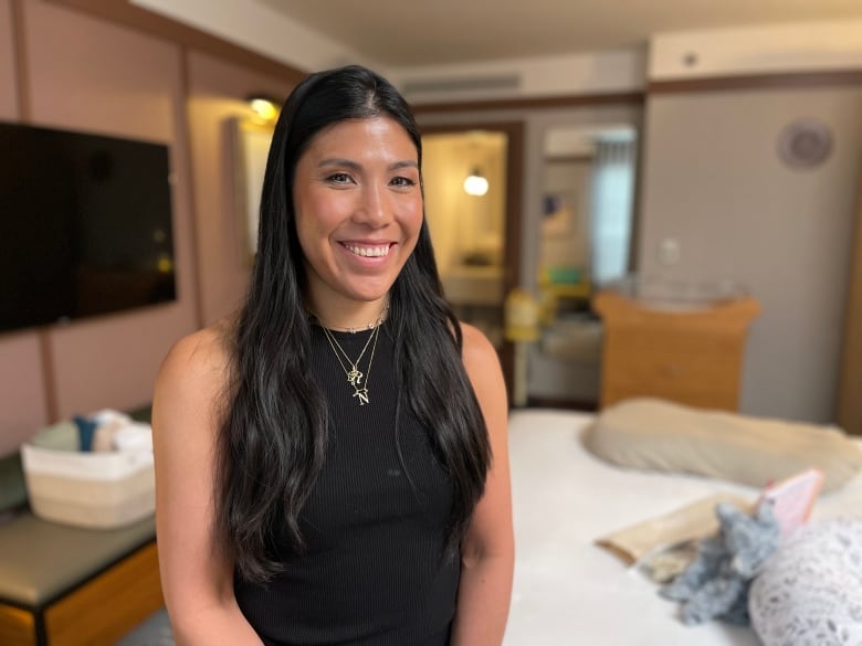 Una mujer con cabello largo y negro y vestida con una camiseta negra aparece de pie dentro de una habitación de hotel de Toronto.