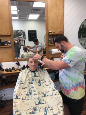 Justin "Murmullo" Murphy corta el pelo a un cliente, Doug Warrick, en la peluquería Kirkland's Barber Shop, en la plaza Lake Miriam. Murphy dijo que la reconstrucción de Publix no ha afectado mucho a su promedio de 12 a 14 cortes de pelo por día.