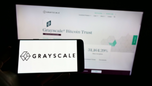 Persona que sostiene un teléfono móvil con el logotipo de la empresa estadounidense de criptomonedas Grayscale Investments LLC en la pantalla frente a una página web. Enfoque en la pantalla del teléfono. Foto sin modificar. Acciones de GBTC