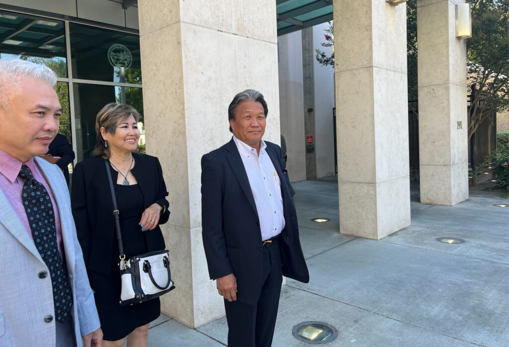 Tres personas, dos hombres y una mujer, de pie junto a un edificio.