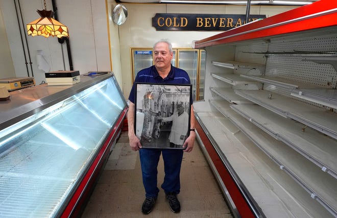 De pie entre estantes vacíos, Joe Agemy, de 65 años y presidente de Agemy & Sons Market, sostiene una fotografía de su padre, Mack Agemy, dentro de la carnicería en Allen Park el martes 27 de agosto de 2024. Agemy aprendió sobre el negocio de la carnicería de su padre cuando era más joven. El mercado, ubicado en medio de un gran vecindario, tuvo su último día de funcionamiento el sábado 24 de agosto de 2024, ya que Agemy planea jubilarse y su hijo tiene su propia carrera.