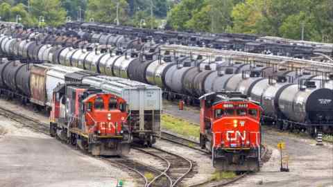 Los vagones de ferrocarril están densamente abarrotados en el depósito de carga de CN Rail en Hamilton, Ontario, Canadá. En primer plano se ven dos locomotoras CN rojas, rodeadas de numerosos vagones cisterna negros y otros vagones de mercancías. Al fondo se ven árboles y vegetación.