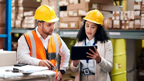 Getty Images Empleados con cascos en un almacén discutiendo sobre negocios mientras miran una tableta