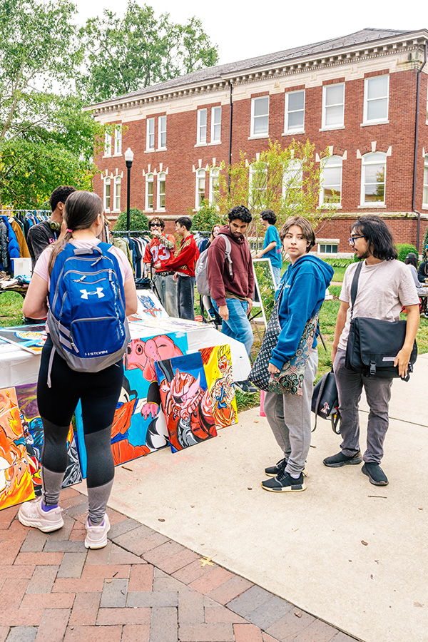 Los estudiantes se reúnen alrededor de obras de arte a la venta en el mercado estudiantil de la UNCG.