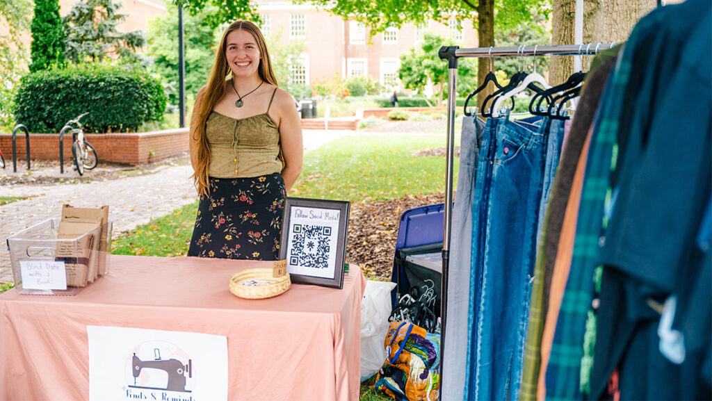 Una estudiante emprendedora de la UNCG sonríe desde su stand lleno de ropa.