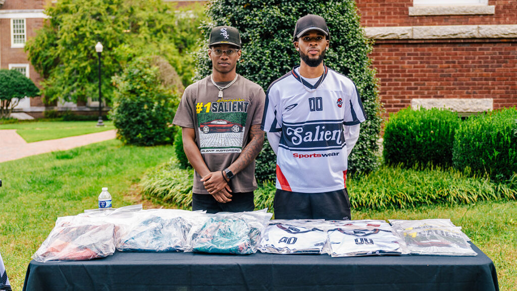 Dos estudiantes de la UNCG se paran frente a las camisetas que venden afuera.