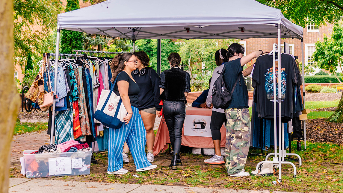 Estudiantes de la UNCG miran ropa en los estantes a la venta en un mercado al aire libre.