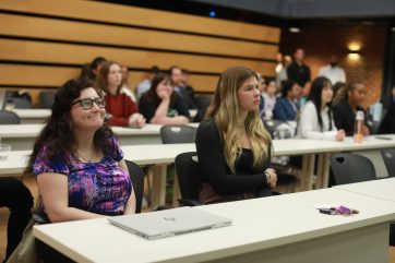 Los estudiantes de negocios de la UMW Alexandria Menzies (izquierda) y Avery Bonner, quienes fueron los primeros en compartir su presentación durante la competencia de casos de la Facultad de Negocios, escuchan mientras otros equipos toman sus turnos. Foto de Karen Pearlman.