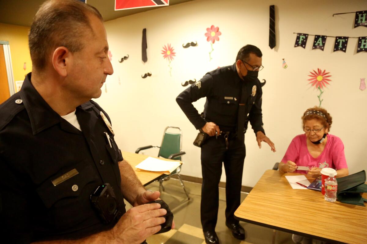 Mientras el oficial principal de LAPD, Carlos Díaz, observa, el detective Albert Smith le deja una tarjeta a Marta Barillas, a quien robaron recientemente.