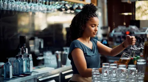 Getty Images Joven camarera sirviendo cerveza de barril mientras trabaja en la barra del bar. 