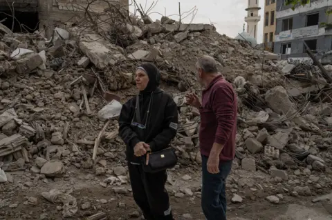 Niran Ali y su marido se encuentran frente a los restos de su tienda de ropa infantil destruida.