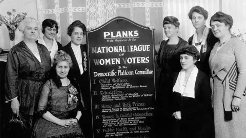 Getty Images Miembros de la Liga de Mujeres Votantes de EE. UU. son fotografiados con una tabla que la organización presentó al Comité de la Plataforma Demócrata en 1920. 